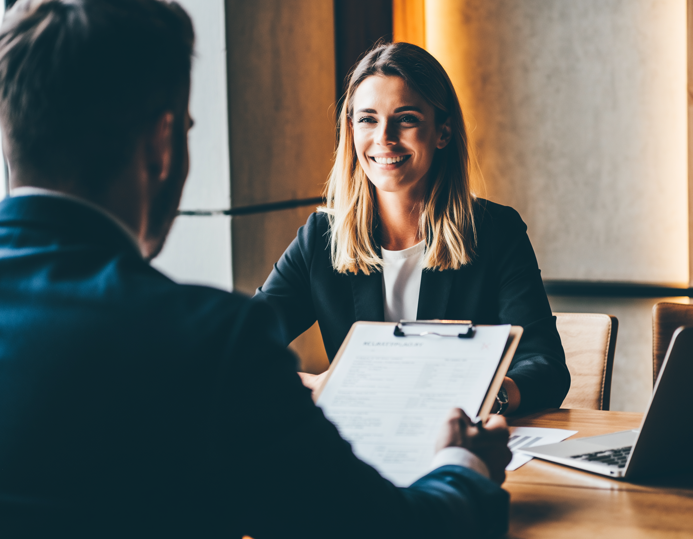 Strukturiertes Kandidatengespräch: blonde Interviewerin (30+) führt freundlich und professionell ein Gespräch mit Leitfaden.